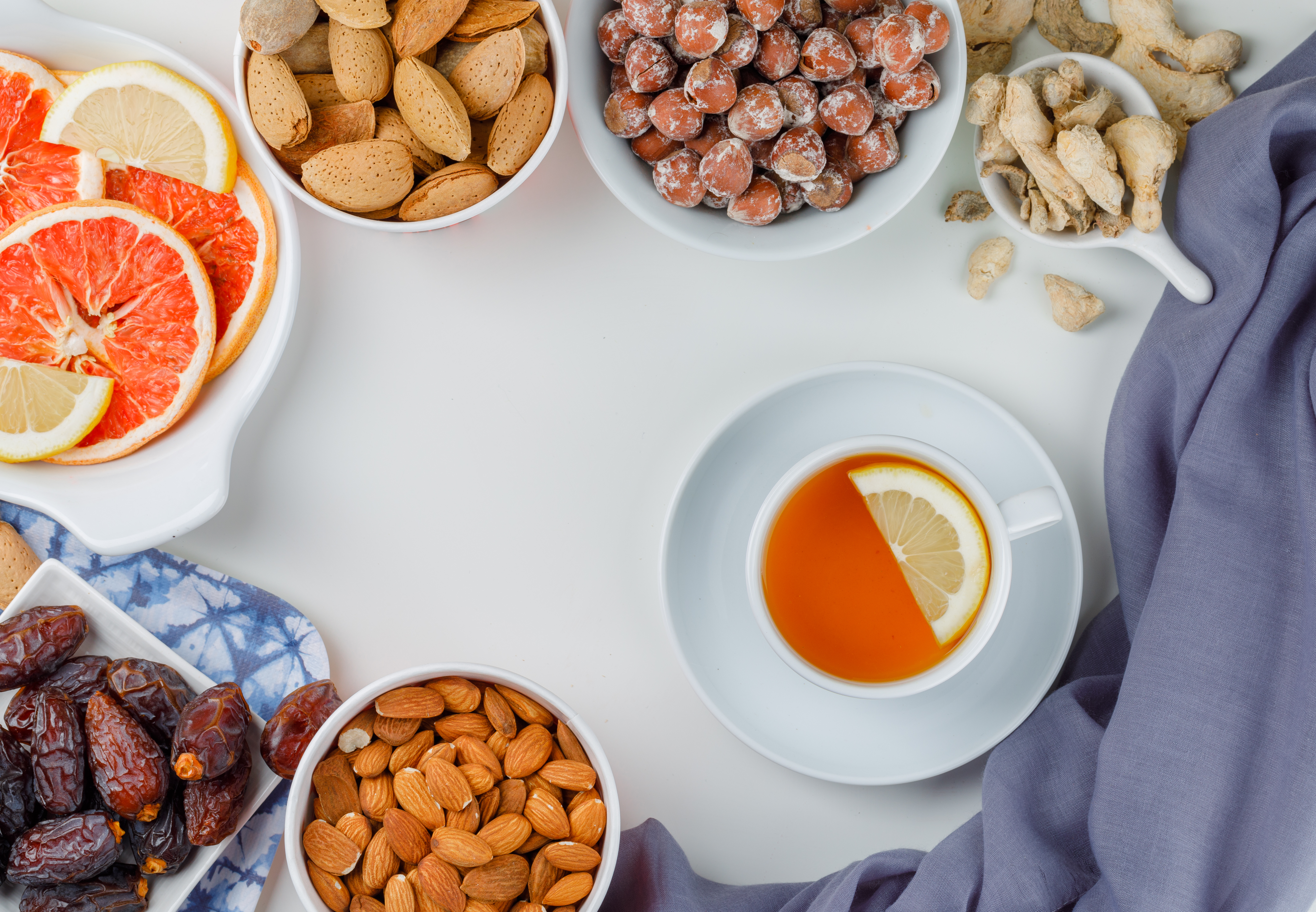 nuts-variety-with-cup-tea-dates-citrus-fruit-slices-ginger-white-plates